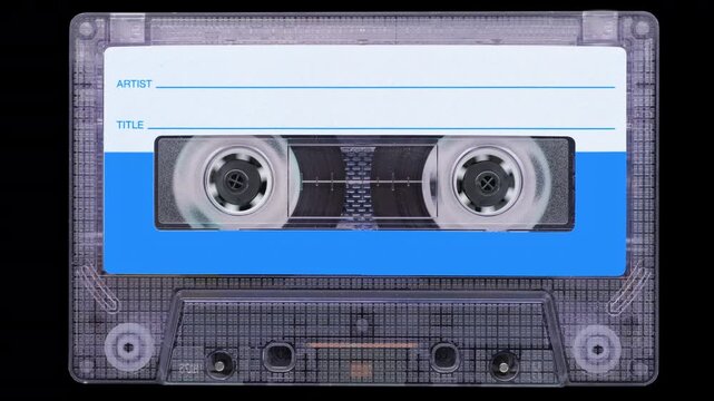 Vintage Compact Cassette with Spinning Reels. Front view of a compact cassette with rapidly spinning reels on black background.