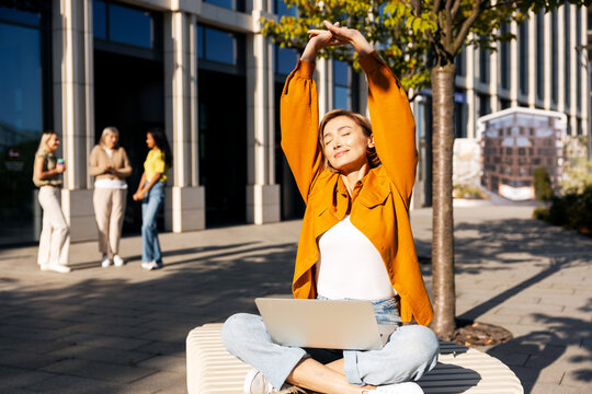 Woman stretching outdoors enjoying sun while remote working