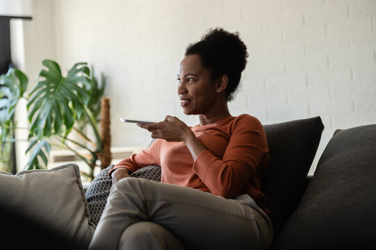Happy woman smiles while talking on a smartphone and relaxing on a sofa at home, enjoying a pleasant phone conversation or good news