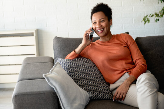 Smiling woman chats on her mobile phone while relaxing comfortably at home, representing friendship, connection and keeping in touch