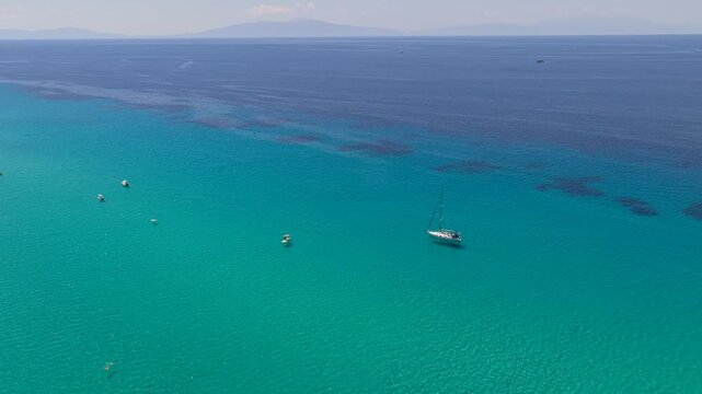Turquoise Greek sea showing an anchored sailboat scattered