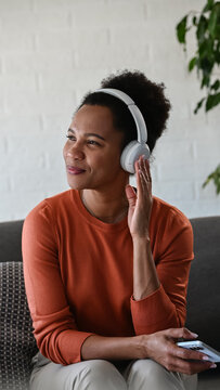 Smiling woman enjoys streaming music on her smartphone with wireless headphones while spending leisure time at home