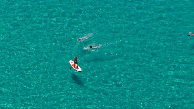 Paddleboarder and swimmers enjoying crystal clear turquoise sea