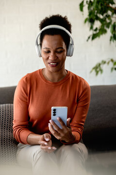 Woman listening to a podcast on her smartphone with wireless headphones while relaxing comfortably at home
