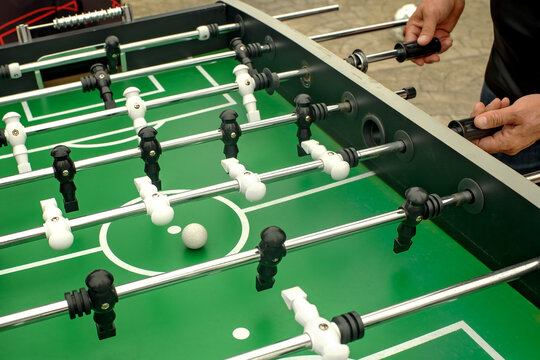 Close up of male hands playing green outdoor foosball table soccer with white dirty ball and dusty lines concept