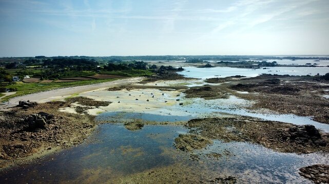 Boats stranded at low tide in Brittany, France. Low tide reveals rocky shorelines and scattered pools in Brittany, France. Boats rest on exposed seabed, surrounded by a mix of sand and rocks. 