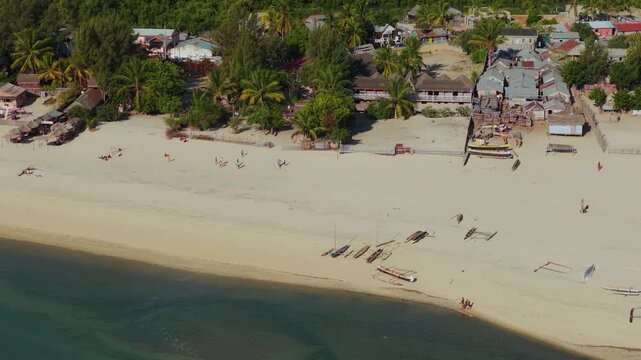 Aerial view of the sandy beach in Morondava with traditional wooden outrigger boats resting on the shore, small coastal houses, and lush palm trees, Morondava, Menabe, Madagascar.