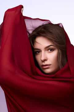 Intense brunette woman framed by rich burgundy fabric wrapped around face and shoulders. Concept of luxury cosmetics, fragrance ads and dramatic editorial.