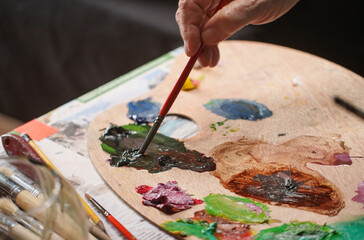 Close-up of senior artist holding a paintbrush and mixing oil colors on a wooden palette © hcarbuccia