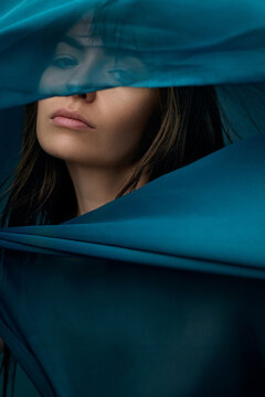Cropped beauty portrait of woman concealed behind translucent teal fabric. Concept of skincare ads, fragrance branding and abstract editorial.