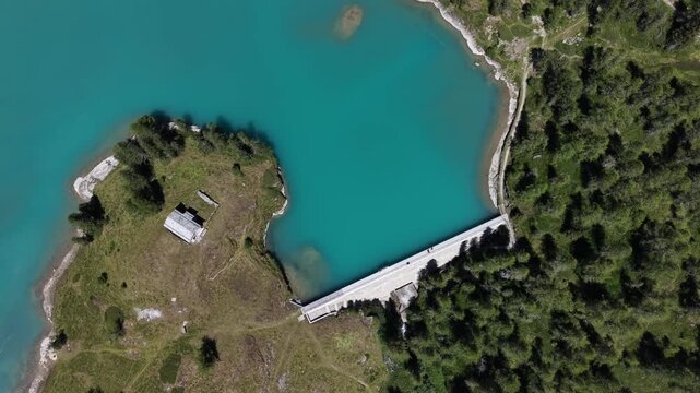 Aerial view of Wasserkraftwerk Palu dam, Hydroelectric power and its turquoise reservoir lake surrounded by dense green forests and alpine terrain in Poschiavo, Grisons, Switzerland.
