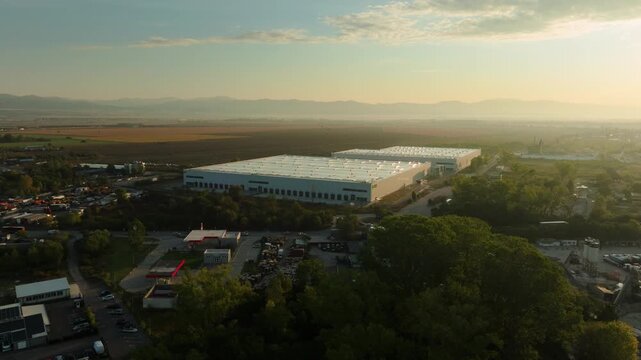 Drone circles warehouse on the outskirts of a city early in the morning, sun gets into the frame