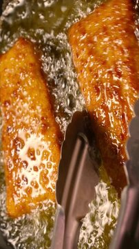 Breaded Cutlets Frying in Hot Oil. Close-up of golden breaded pieces sizzling in bubbling oil while metal tongs turn them.