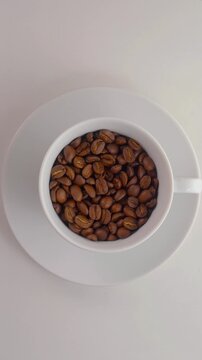 Rotating Coffee Beans in Cup Seamless Loop. Top view of a white cup filled with roasted coffee beans rotating smoothly on a saucer.
