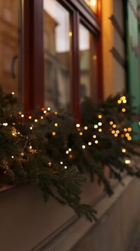 Atmospheric video of warm golden Christmas string lights illuminating outside a window pane during winter holidays at night.
