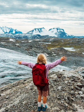 Child girl hiking mountains in Norway family travel vacations outdoor tour, 5 years old kid scout with backpack happy raised hands enjoying Smorstabbreen glacier view explore Jotunheimen trails