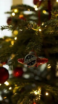 Close up shot of a retro toy plane bauble decorating a green Christmas tree branch with warm glowing holiday fairy lights in the background.