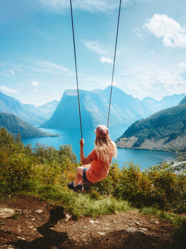 Woman tourist travel in Norway swinging with fjord and mountains view, girl traveler having fun outdoor active vacations hiking adventure tour in Sunnmore Alps explore beautiful travel destination