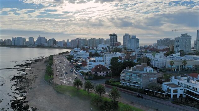 Punta del Este aerial view of Playa Mansa beach and coastal urban skyline with palm trees, clear ocean, and road in slow motion.