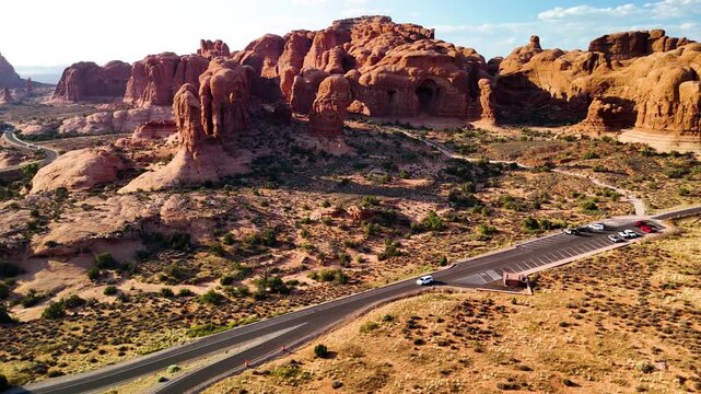 Stunning stock footage of Arches National Park USA during a bright afternoon. The brilliant sunlight illuminates the majestic red rock sandstone structures and desert landscape under a clear blue sky.