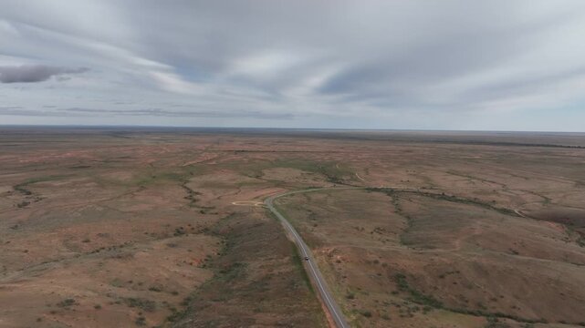 High aerial drone tracking shot following a vehicle along a winding remote road through the vast outback landscape near Silverton and Broken Hill, New South Wales, Australia.