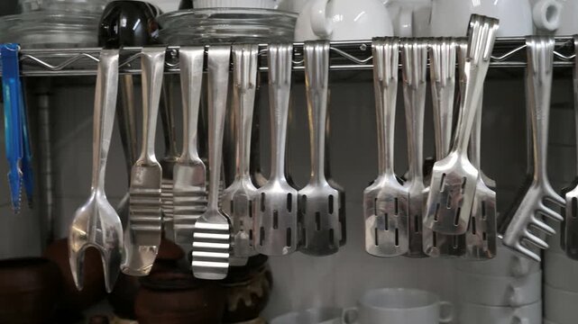 Stainless steel kitchen utensils including ladles, grater, and cleaver hanging on a metal rack in a professional restaurant kitchen.