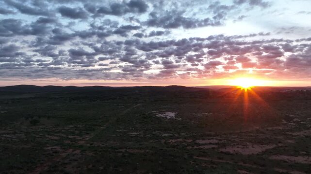 Dramatic aerial sunset over the rugged outback landscape surrounding Broken Hill, with the setting sun breaking through scattered clouds in far western New South Wales.
