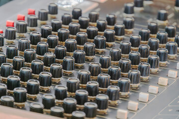 Obraz premium Close-up view of professional audio mixing console with black faders and white labels, featuring red accent knobs, slightly worn surface indicating use, high-quality equipment for music production and