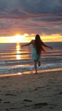 Silhouette woman walking into shallow surf at sunset, arms lightly spread as small wave meets her step over wet sand, glowing reflection, warm rim light, peaceful coastal scene, with silhouette