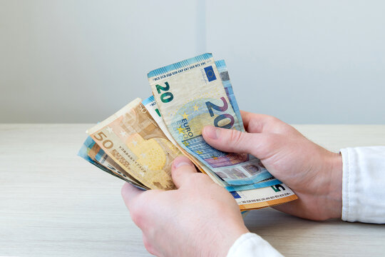 A close-up of a man's hands counting a stack of euro banknotes. Successful business deals, cost control, debt repayment, lending, borrowing money, corruption, bribery