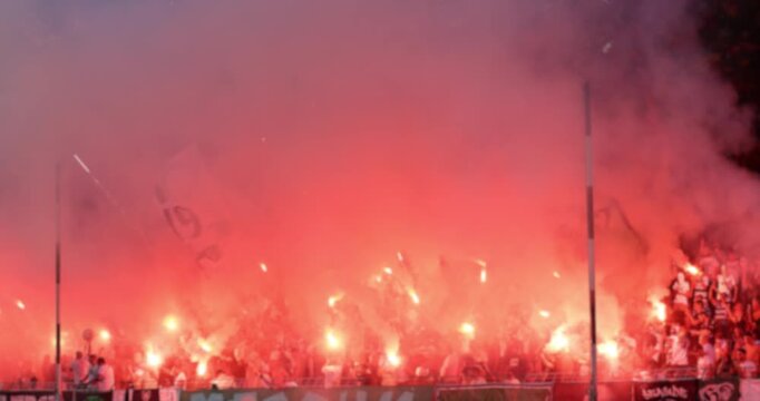 Passionate football fans with smoke bombs, fire torch and flares at a stadium. Ultras creating an intense, chaotic atmosphere with pyrotechnics during a night match or protest.