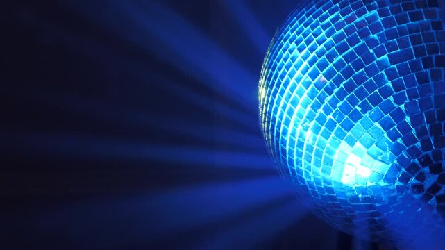 Shiny mirror disco ball with multicolored light rays in the background.