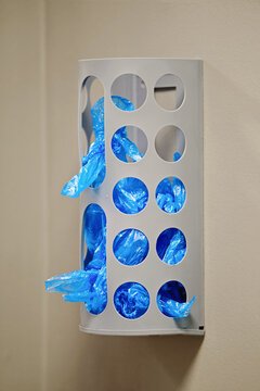Shoe cover dispenser organizer stocked with blue plastic disposable overshoes. Wall mounted grey plastic shoe cover dispenser filled with disposable booties attached to beige interior. Selective focus