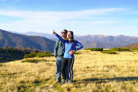 Couple stands against backdrop of Montenegrin highlands, woman pointing at something. Depicts shared adventure holidays, decision-making, upward aspiration, and mountain escapes beyond crowded resorts