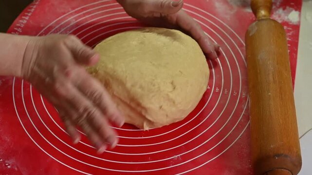 Woman hands shaping dough into round form on silicone baking mat. Dough pressed and folded gently, dough becoming smooth and elastic, close-up home baking process, bread preparation concept