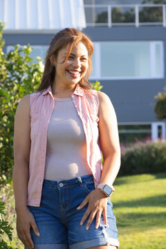 African American woman standing near shrubs in front yard of house wearing denim shorts, smartwatch