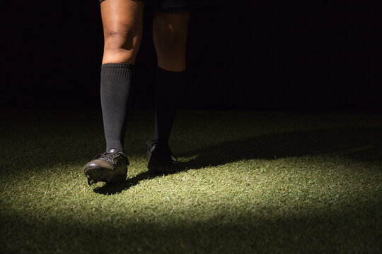 Female soccer player standing on turf at night wearing knee-high socks and cleats under spotlight