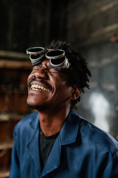 Man wearing welding goggles smiles in workshop