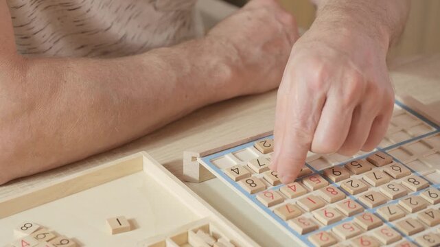 closeup hands carefully placing number into Sudoku puzzle, senior man focused on solving puzzle on wooden board, Brain exercise, cognitive health, and mental agility in mature age, brain health