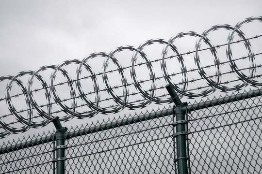 A barbed wire fence with sharp razors on top, suitable for use in crime scene or prison themed images