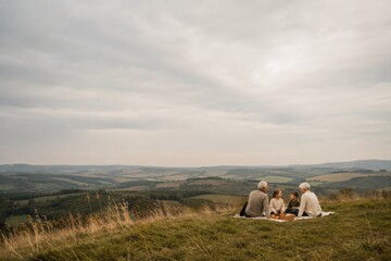 Fototapeta premium Grandparents and Grandchildren Sharing Picnic on Open Grassy Hill