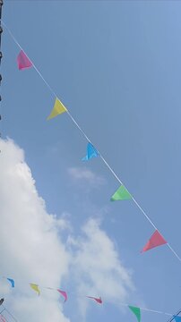 A string of colorful triangular flags stretches across the clear blue sky. Pink, yellow, blue, green, and red flags can be seen fluttering in the wind.