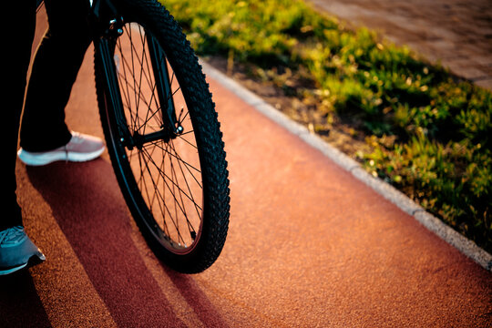 Close up of bicycle wheel on red sports track during golden hour. Cycling gear, active movement concept, urban transport.