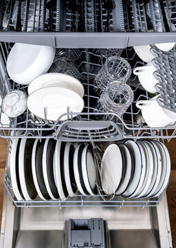 Open dishwasher loaded with clean dishes, glasses and cups in a modern kitchen.