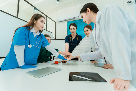 Medical team of doctors and nurses stacking hands in unity during clinic meeting