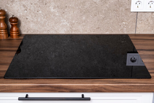 Modern induction cooktop built in wooden countertop in minimalist kitchen. Clean induction stove hob, modern kitchen interior, kitchen appliance design, modern home concept.
