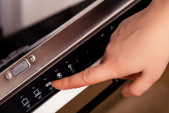 Woman hand pressing eco button on dishwasher control panel. Concept of energy saving technology.