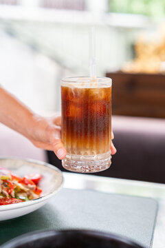 Close up of woman hand lifting glass of iced espresso tonic