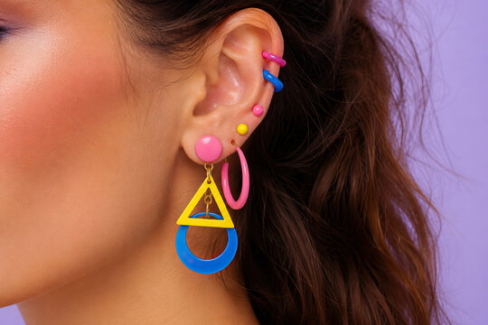 A young woman's ear is dramatically highlighted with vibrant geometric earrings. High-resolution photograph focusing on a person's ear adorned with colorful jewelry.