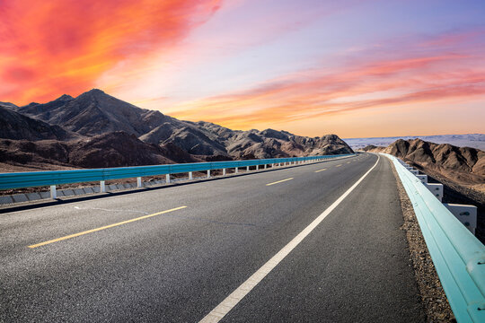 Empty asphalt road stretching through a mountainous desert landscape under a sunset sky in Qinghai, China